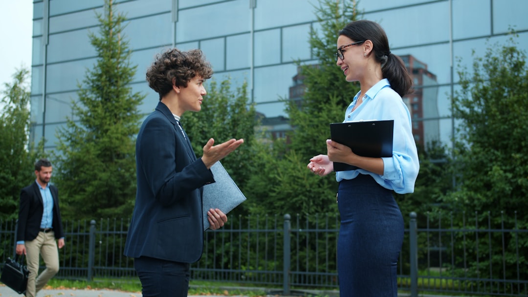 Female entrepreneurs young women are chatting outdoors shaking hands saying good-bye and leaving in city in summer. Communication and corporate culture concept.